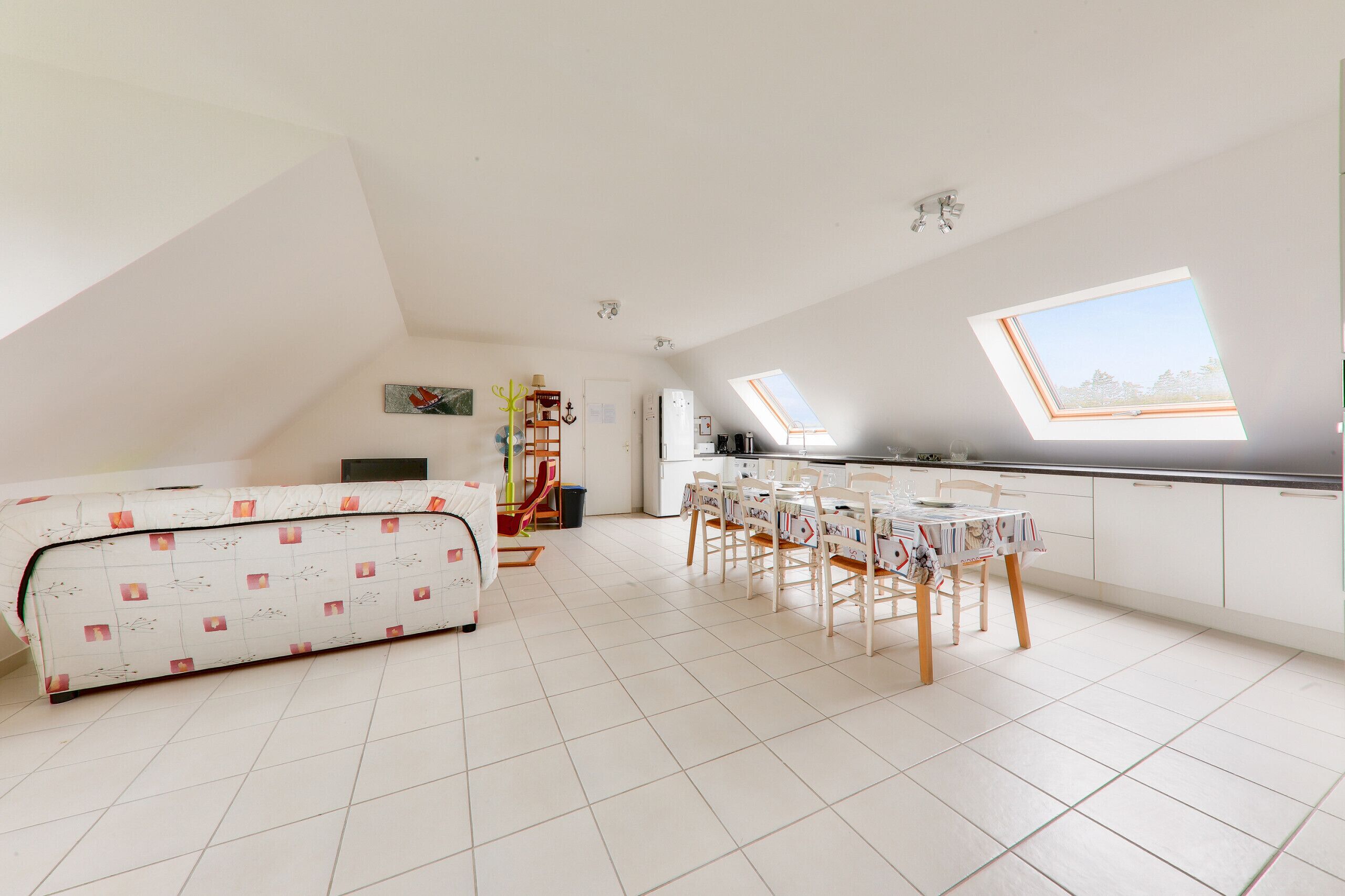 A spacious room with a high ceiling, a skylight, a dining area with a table and chairs, and a sofa.