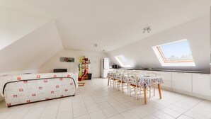Una habitación amplia con techo alto, tragaluz, zona de comedor con mesa y sillas, y un sofá.
