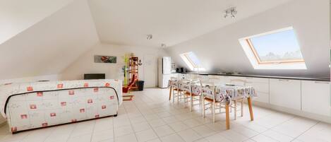 A spacious room with a high ceiling, a skylight, a dining area with a table and chairs, and a sofa.