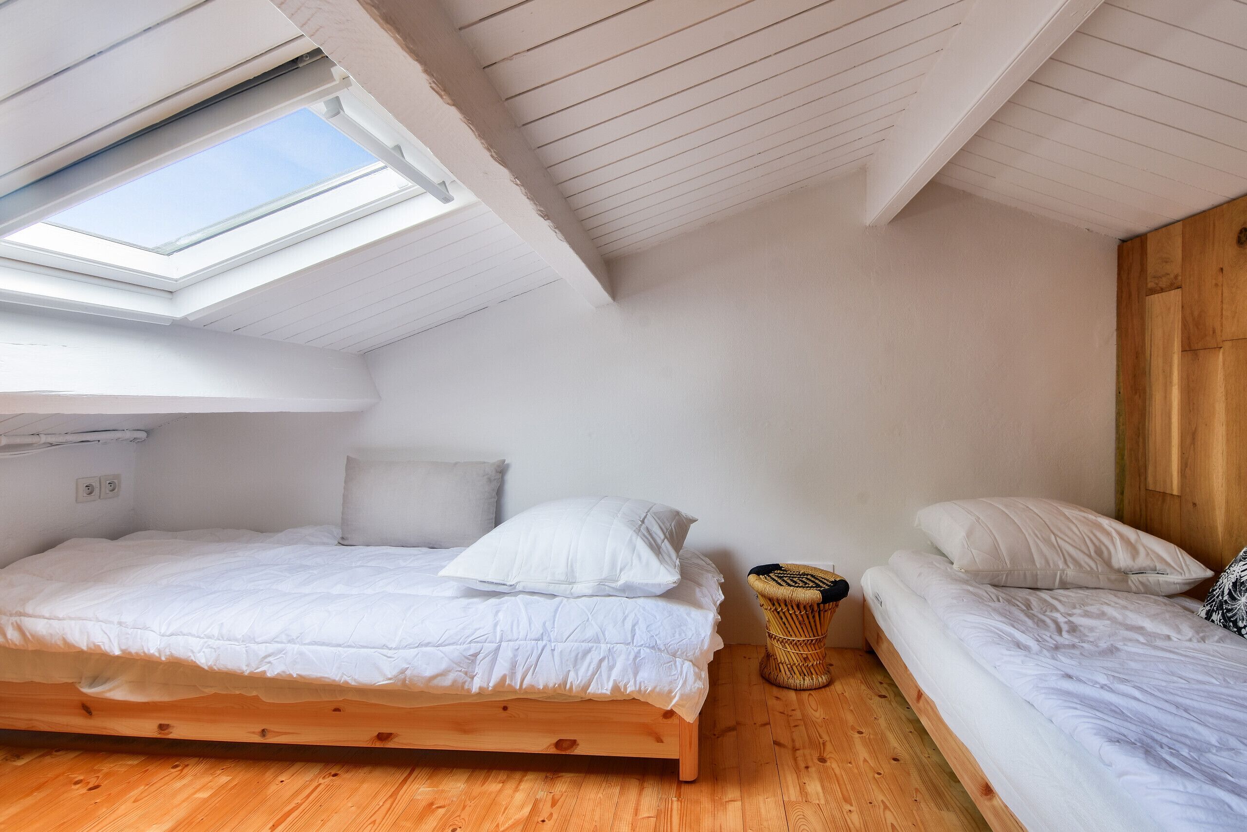 Een lichte, compacte kamer met twee bedden, een dakraam en houten vloeren.