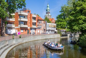 Ein Kanal mit einem Boot, das Fahrgäste befördert, umgeben von Gebäuden mit einer Mischung aus moderner und traditioneller Architektur, darunter ein markanter Kirchturm.