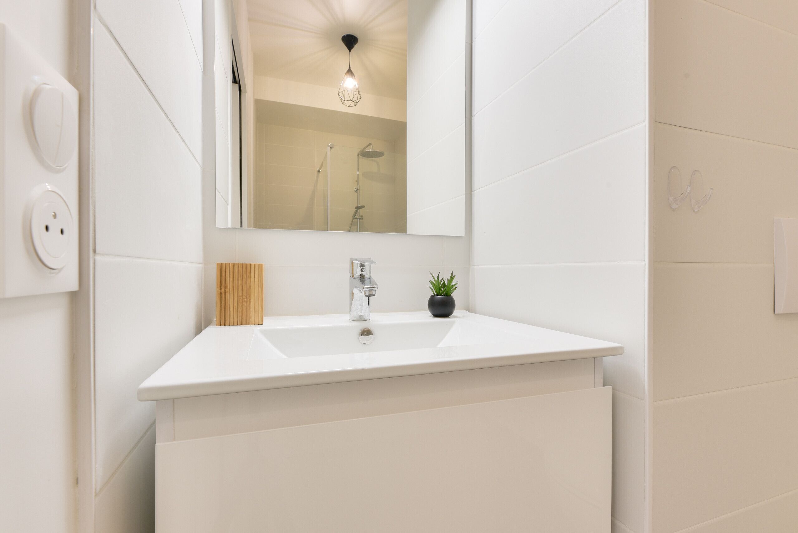 A modern bathroom with a white sink, a mirror, and a small potted plant.