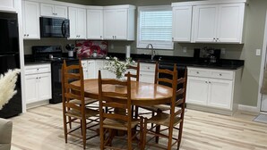 Una cocina moderna con armarios blancos, un refrigerador negro, un microondas y una mesa de comedor con sillas.