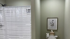 Un baño con cortina de ducha, inodoro y un cuadro en la pared.