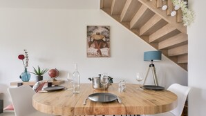 Un comedor con una mesa redonda de madera, sillas blancas y rosas, un globo terráqueo, una planta en maceta y un cuadro en la pared.