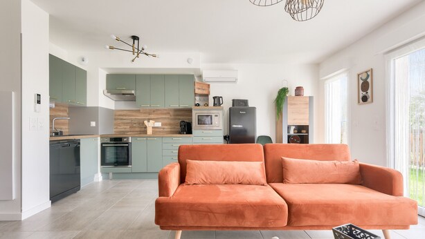Una cocina moderna con armarios verdes, piso en dos tonos y un sofá naranja grande en la sala.