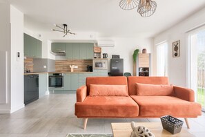 A modern kitchen with green cabinets, a two-tone floor, and a large orange sofa in the living area. - Pretty house with terrace in Andernos-les-bains (Andernos-les-Bains)