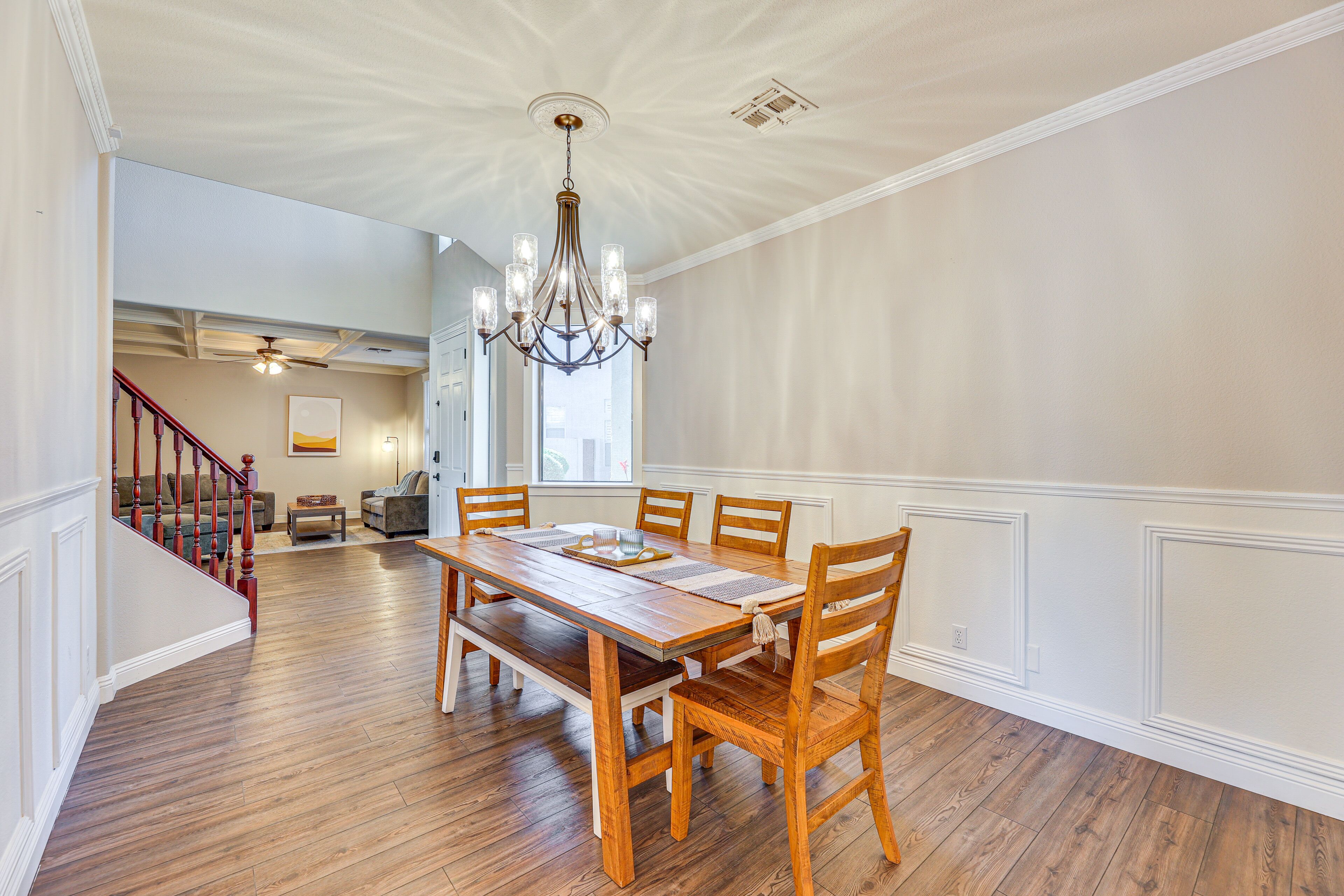 A dining area with a wooden table and chairs, a chandelier, and a staircase leading to another room.