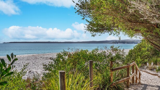 A beach with a wooden fence and greenery in the foreground, leading to a sandy shore and calm sea. - Sandpiper, Hyams Beach, Jervis Bay (Hyams Beach)