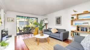 A living room with a grey sofa, a round coffee table, and a bookshelf. - Sandpiper, Hyams Beach, Jervis Bay (Hyams Beach)