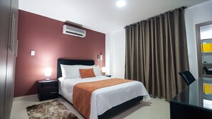 Una habitación de hotel con cama, mesitas de noche, escritorio y espejo.