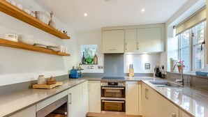 A modern kitchen with built-in appliances, wooden shelves, and a window with a view. - 2 bedroom accommodation in Much Hadham (Much Hadham)