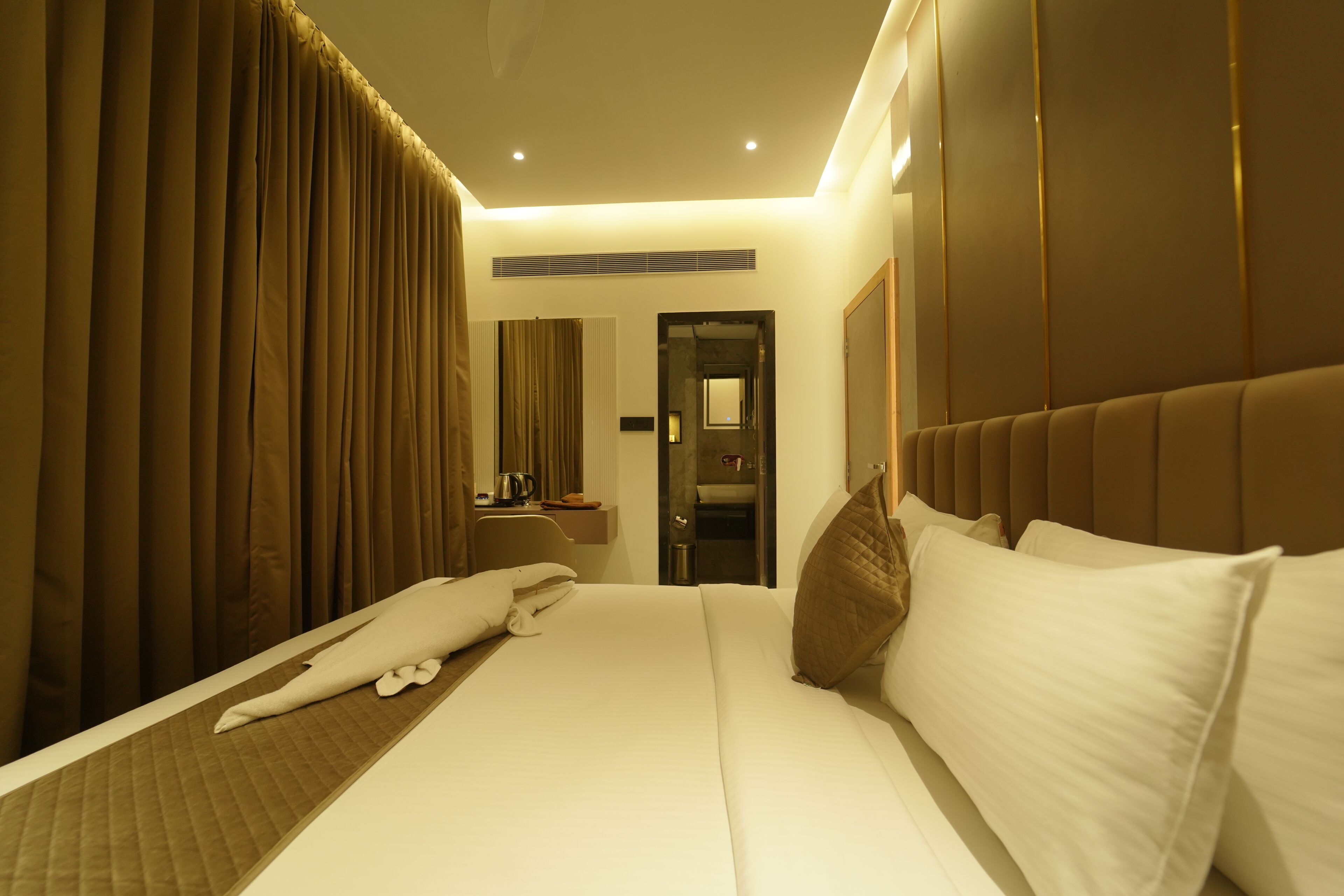 A hotel room with a large bed, a bedside table, a mirror, and a door leading to a bathroom.