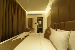 A hotel room with a large bed, a bedside table, a mirror, and a door leading to a bathroom. - Yuvraj Le Royale (Mysore)