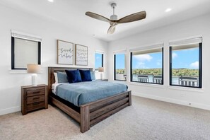 A bedroom with a large bed, a ceiling fan, and multiple windows offering a view of the outdoors. - Lone Star Landing | Concierge Services (Kingsland)