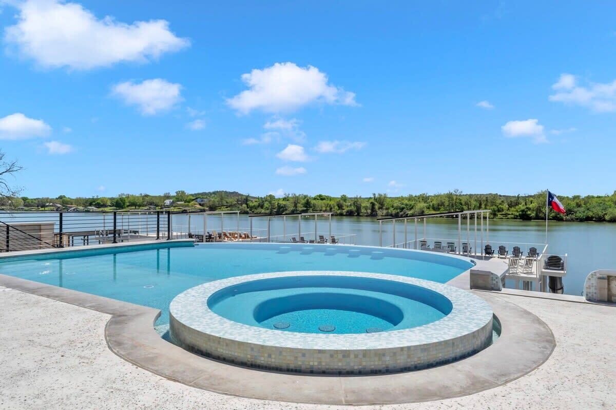 Une piscine avec un jacuzzi circulaire au centre, entourée de chaises longues et offrant une vue sur un lac.