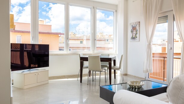A modern living room with a sofa, a glass coffee table, a TV, and a dining area with chairs and a table. - Roma per te - One Bedroom Apartment, Sleeps 4 (Rome)