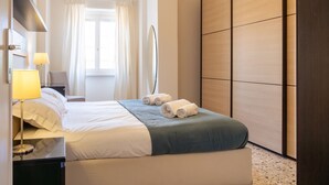 A hotel room with a bed, a bedside table with a lamp, a wardrobe, and a window with curtains. - Roma per te - One Bedroom Apartment, Sleeps 4 (Rome)