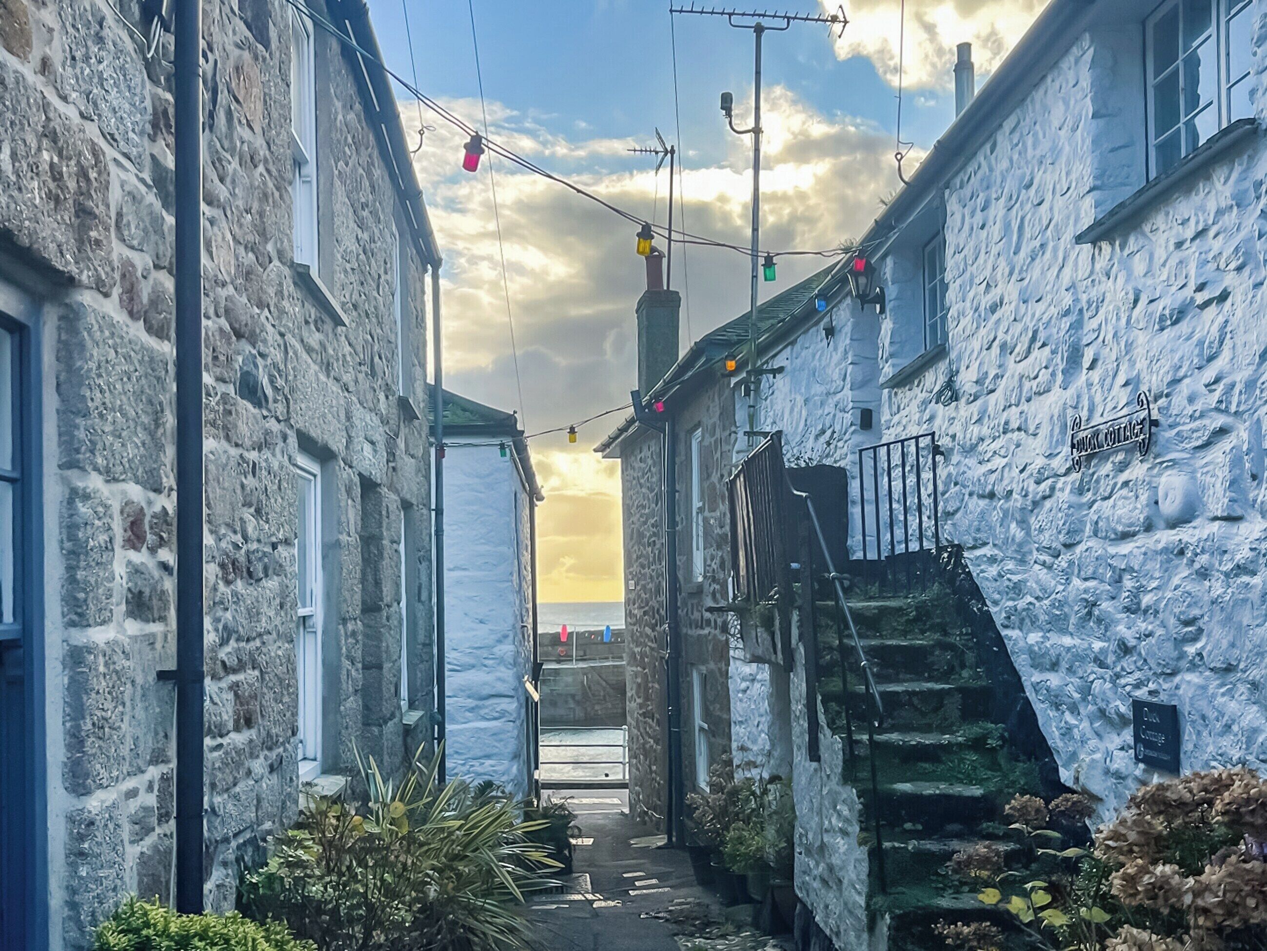 Uma estreita passagem de pedra com uma escadaria que leva a um edifício com a placa 'Fox Cottage'.