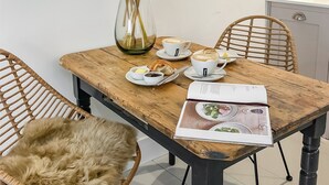 Een houten eettafel met twee witte kopjes, een bord met croissants, een klein kommetje boter en een menukaart.