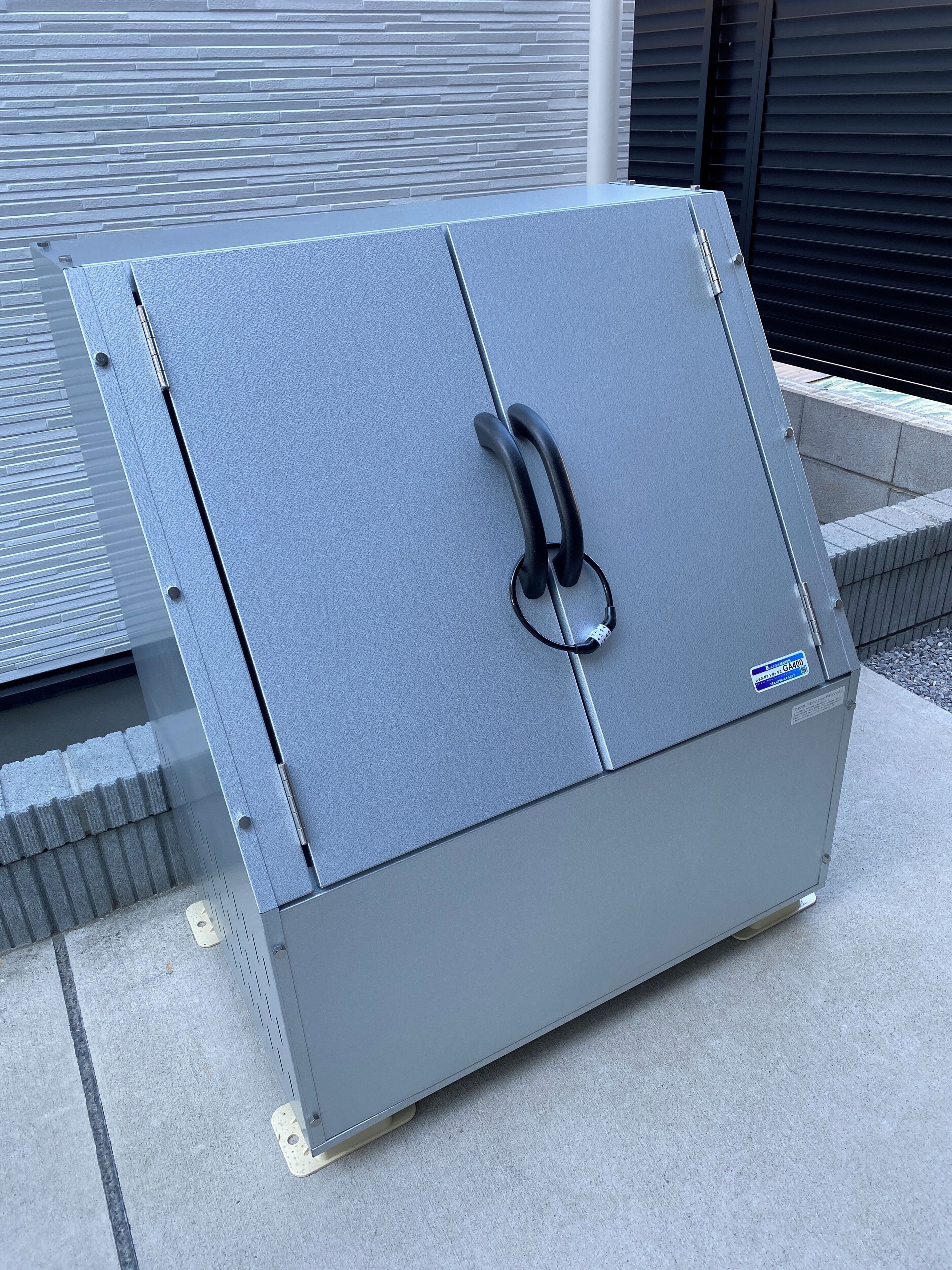 Una caja fuerte metálica gris con asa, ruedas y una placa de matrícula.