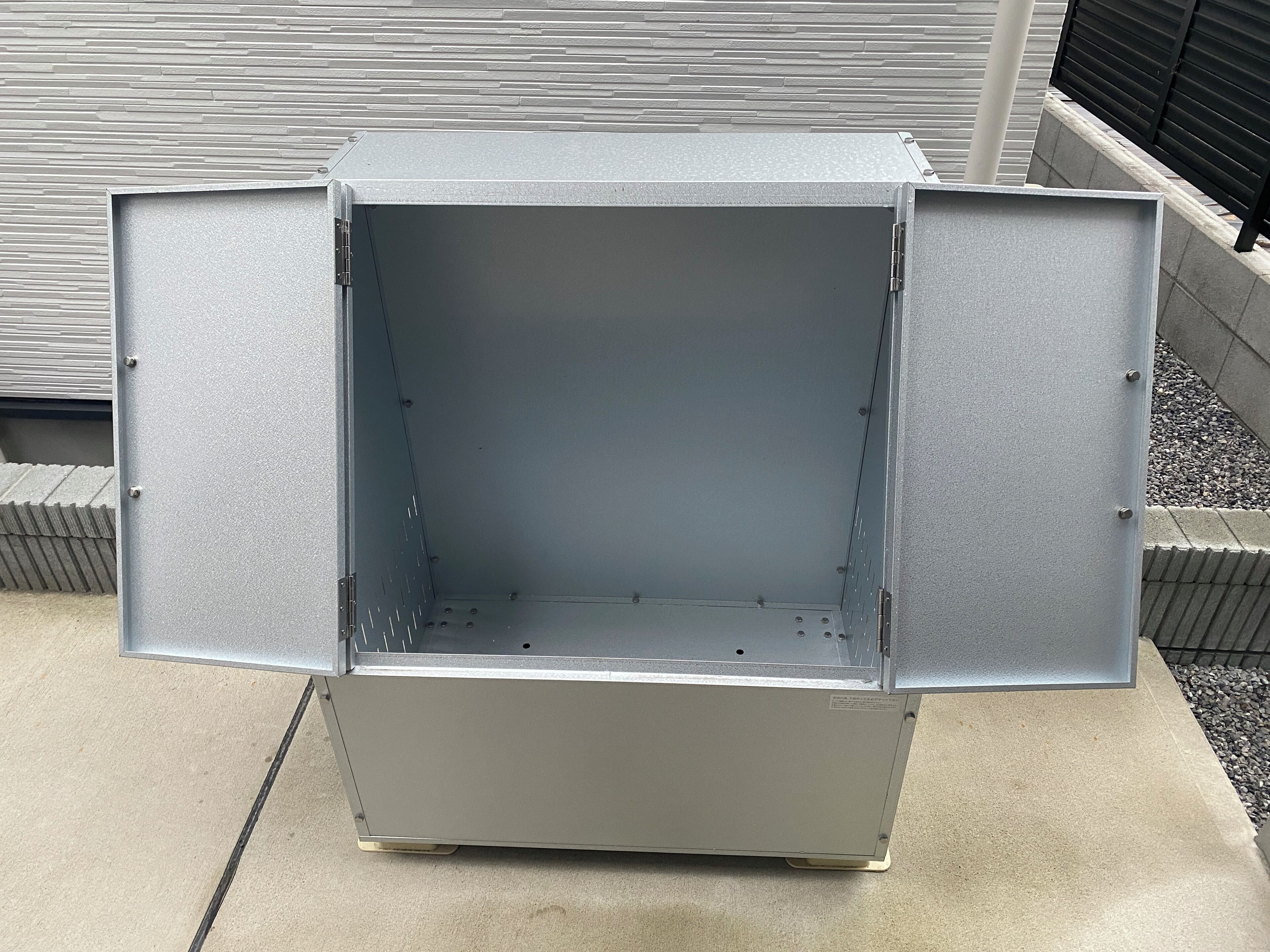 A metal utility box with an open door, located outdoors on a concrete surface.