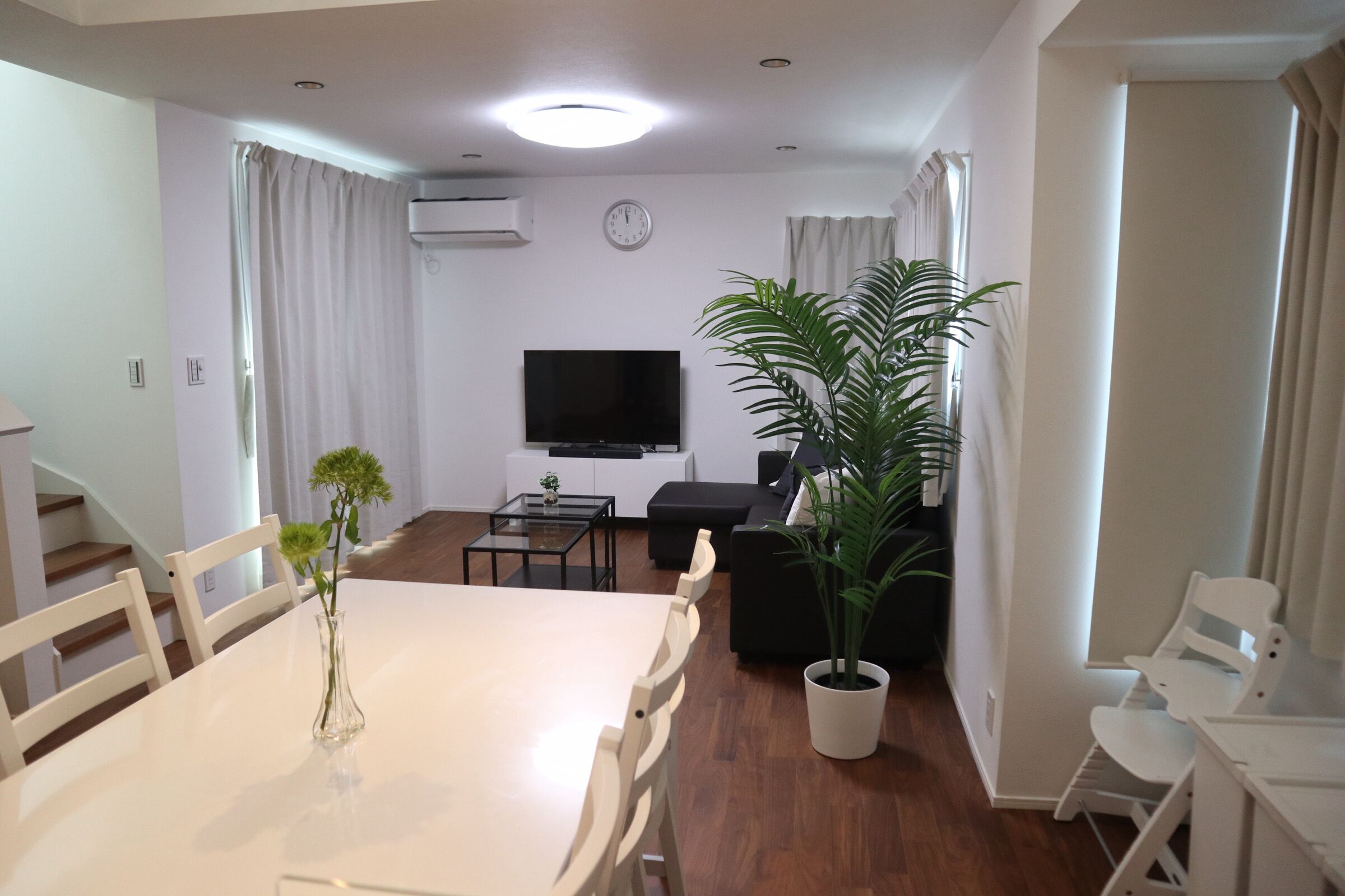 Un salon moderne comprenant une table à manger, des chaises, un canapé, un téléviseur et des plantes en pot.