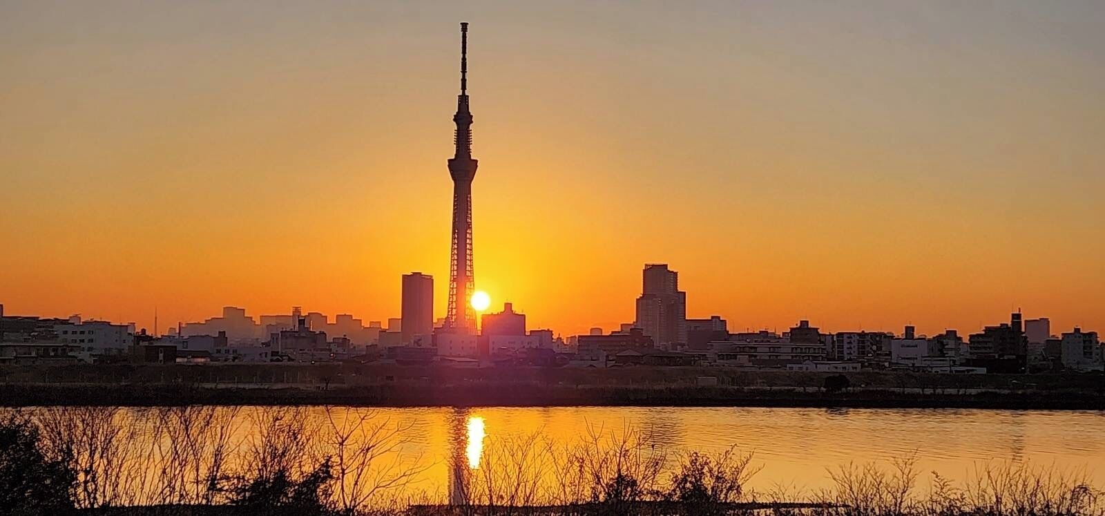 Horizonte urbano al atardecer, con una torre destacada reflejada en el agua.