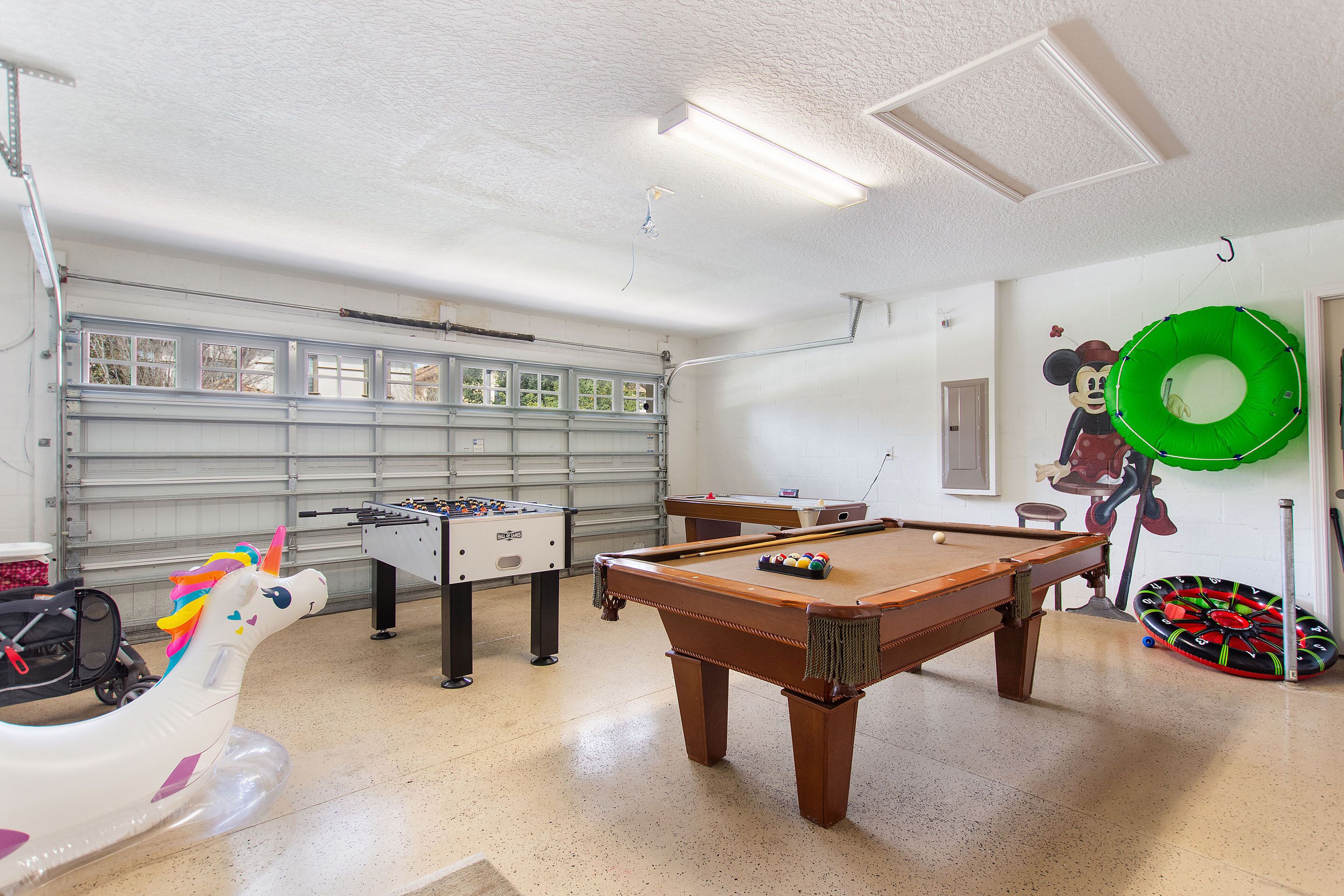 Une table de billard, une table de baby-foot et une licorne gonflable dans une pièce dotée d’une porte de garage et d’un anneau gonflable vert.