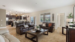 A spacious living room with a large brown leather sofa, a glass coffee table, and a beige sofa. There is a kitchen in the background with dark cabinets and a dining area. - 6 Bed South Facing Pool Resort and Games Room (Davenport)