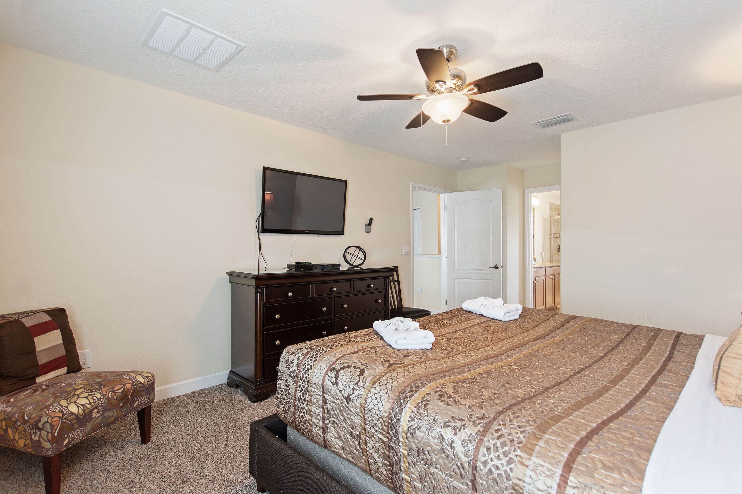 A bedroom with a bed, a ceiling fan, a dresser, a TV, and a chair.