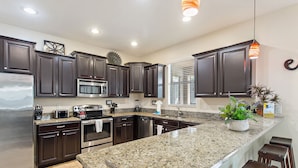A modern kitchen with dark wood cabinets, granite countertops, stainless steel appliances, and a central island with bar stools. - 6 Bed South Facing Pool Resort and Games Room (Davenport)