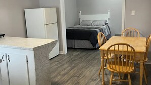 Een compacte kamer met een bed, een kleine keukenhoek en een eethoek met houten stoelen.