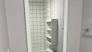 Een badkamer met een wit wastafelmeubel, een spiegel en een betegelde douchehoek.