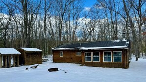 A wooden cabin with a snow-covered roof, surrounded by a forest. - Cozy Cabin- Close to all up North activities! Cabin in Irons. (Irons)