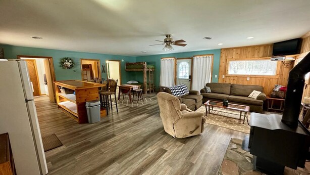 A spacious living area with a wooden floor, a sofa, a chair, a coffee table, and a kitchen area with a refrigerator and a sink. - Cozy Cabin- Close to all up North activities! Cabin in Irons. (Irons)