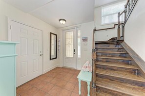 A hallway with a wooden staircase, white doors, and a tiled floor.
