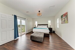 A bedroom with a large bed, a bench, a ceiling fan, and a view of the outdoors. - Spacious Oasis - 3BR Pool Home - By Island Real Estate (Holmes Beach)