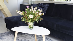 Un salon avec un canapé bleu foncé, une table basse blanche et un vase rempli de fleurs.