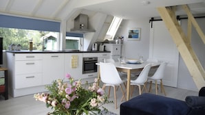 Une cuisine moderne avec des meubles blancs, un coin repas avec des chaises blanches et un escalier.