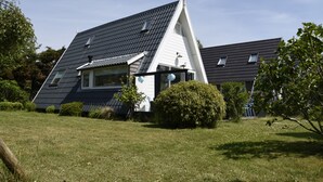 Une maison avec un toit en pente, une cheminée bien visible et une pelouse bien entretenue.