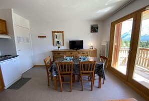 A dining area with a table, chairs, a television, and a view of mountains through large windows. - 200m from ski slopes, 3rd floor, view mountain, tv, ski locker, 32m², Superdévoluy (Le Dévoluy)