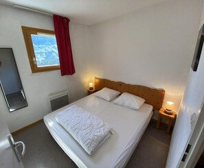 A single bed with a wooden headboard, two bedside lamps, a window with a view, and a mirror on the wall.