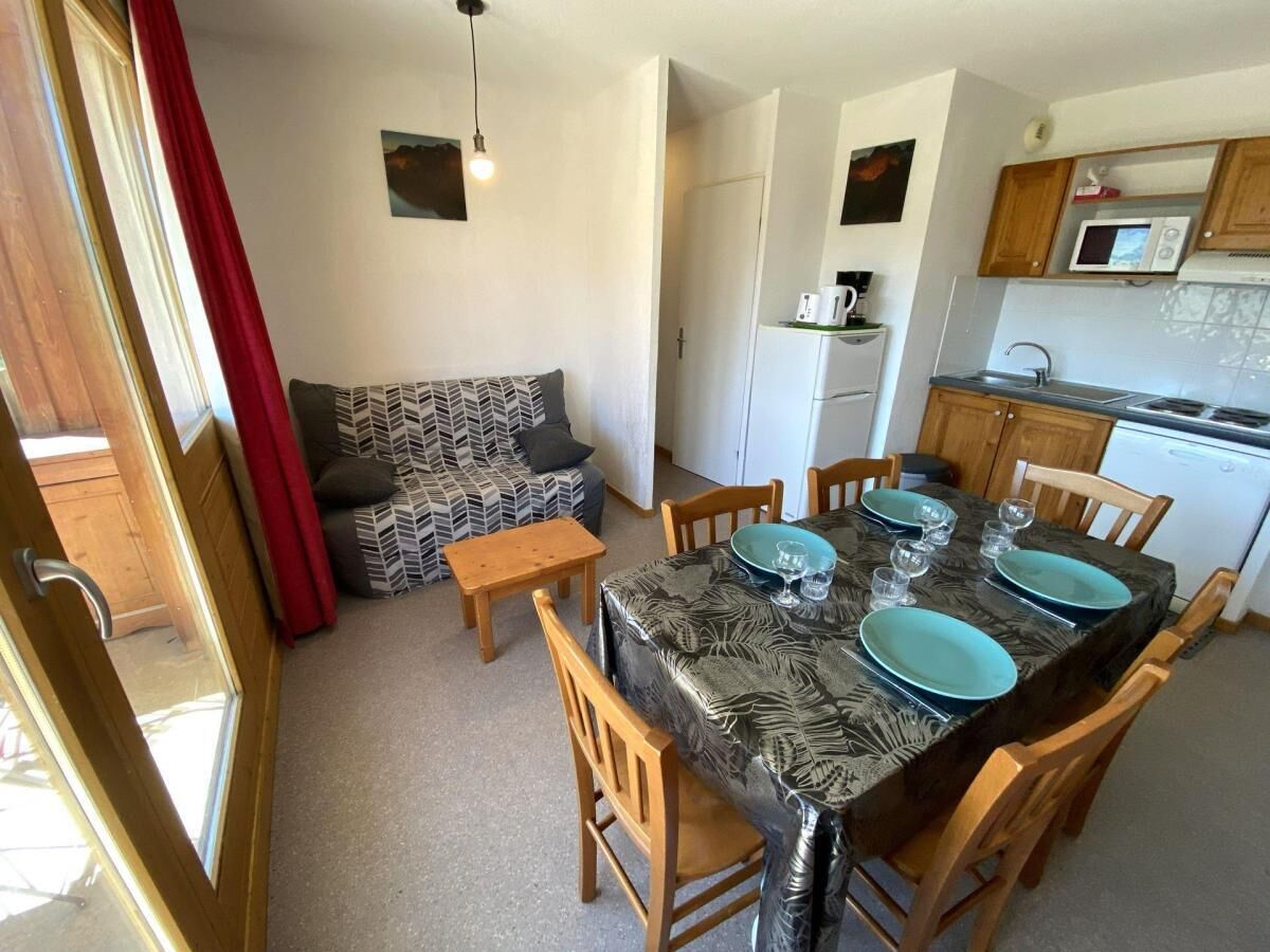 Zona pranzo con tavolo apparecchiato per quattro, cucina con forno a microonde e divano con cuscini decorati.