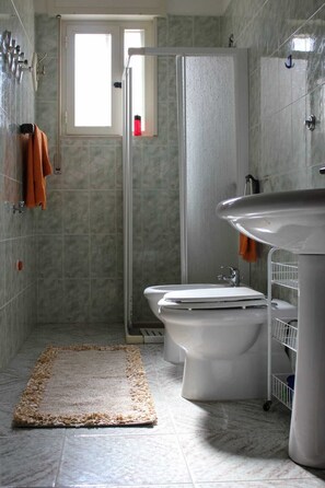 A bathroom with a shower, two toilets, a sink, and a towel rack.
