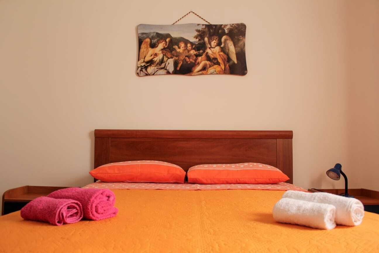 Una habitación de hotel con una cama de madera, ropa de cama naranja, dos almohadas y toallas enrolladas.