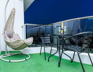 En balkon med en hængekøjsstol, et bord med to stole og en flaske champagne.