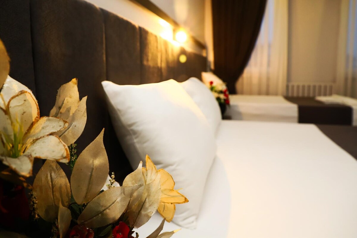 Una habitación de hotel con una cama bien hecha, un ventanal con cortinas y una lámpara de pared.