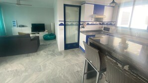 A modern kitchen with a microwave, stove, and sink. There is a dining area with a table and chairs. A television is on a stand in the living area. - Canal Salinas 1º ático Solo Familias! (Xeraco Playa)