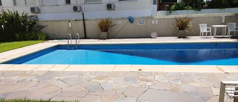 A rectangular swimming pool with a stone border, surrounded by a grassy area and potted plants.